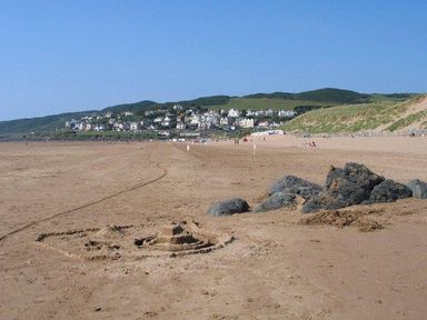 A sandy beach with a sandcastle and rocks with houses and hills in the background at Fairways in Woolacombe