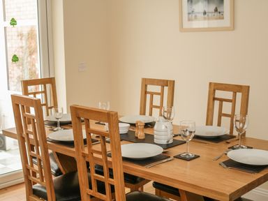 A dining room with a wooden table set with plates glasses and cutlery at Fairways in Woolacombe