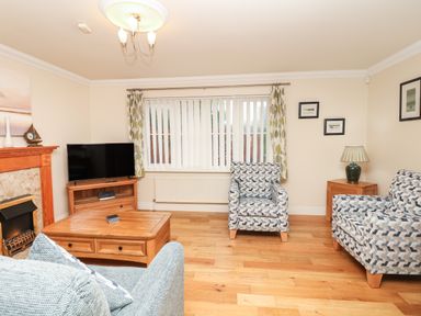 A living room with patterned armchairs wooden coffee table television and fireplace at Fairways in Woolacombe