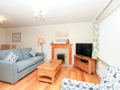 A living room with a blue sofa two patterned cushions wooden coffee table wooden cabinet with a television and a fireplace at Fairways in Woolacombe