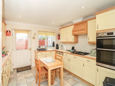 A kitchen with a small wooden table and two chairs a sink a window a door oven and stovetop at Fairways in Woolacombe