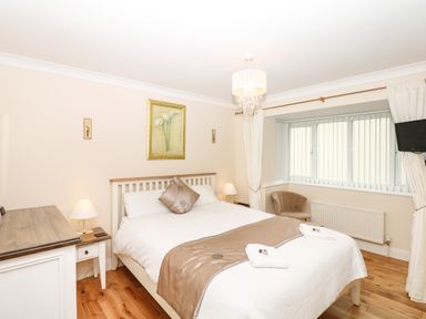 A bedroom with a bed two lamps a chair a dresser and a window with vertical blinds at Fairways in Woolacombe