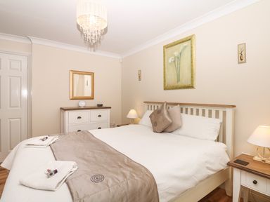 A bedroom with a bed pillows bedside table lamps and a chest of drawers with a mirror at Fairways in Woolacombe