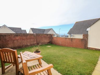 A small garden with a wooden table and two chairs next to a brick wall at Fairways in Woolacombe