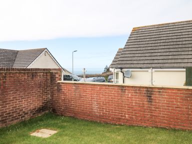 A small grass yard enclosed by red brick walls with houses and cars in the background at Fairways in Woolacombe