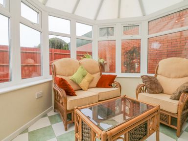 A conservatory with wicker chairs and a glass top table at Fairways in Woolacombe