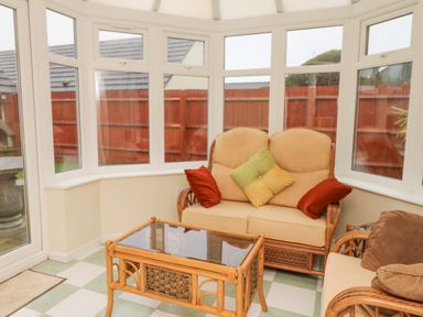 A conservatory with wicker sofa and armchair with cushions and a wicker coffee table at Fairways in Woolacombe