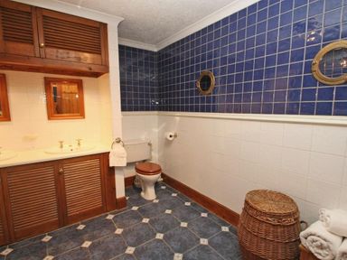 A bathroom with a sink and wooden cabinets a toilet and a wicker laundry basket at Mengarth in Cadgwith