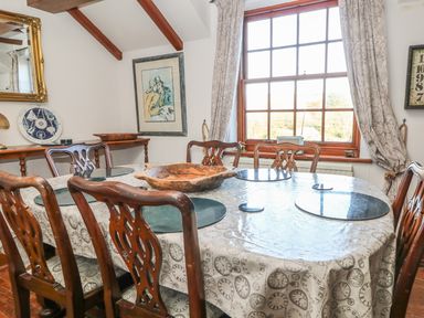 A dining room with a wooden table and chairs and a large window with curtains at Mengarth in Cadgwith