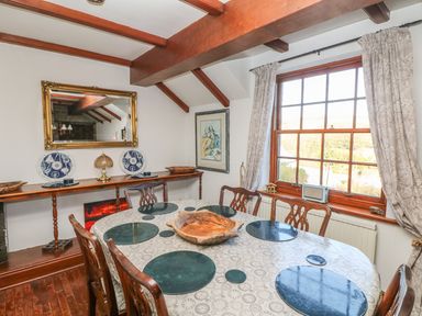 A dining room with a wooden table covered with a tablecloth and seating six chairs at Mengarth Cadgwith