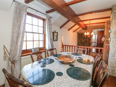 A dining area with wooden chairs round table set with black placemats and decorative bowl wooden beams on ceiling Mengarth Cadgwith