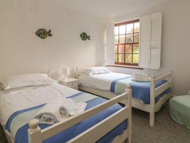 A bedroom with two single beds with blue and green bed runners next to a window at Mengarth in Cadgwith