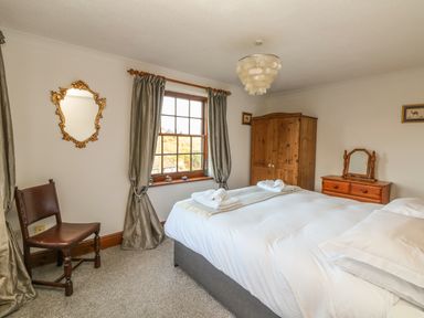 A bedroom with a double bed towels on bed a wooden wardrobe chair and a mirror at Mengarth in Cadgwith
