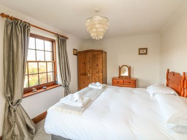 A bedroom with a bed towels on the bed wooden wardrobe and dresser with mirror at Mengarth in Cadgwith