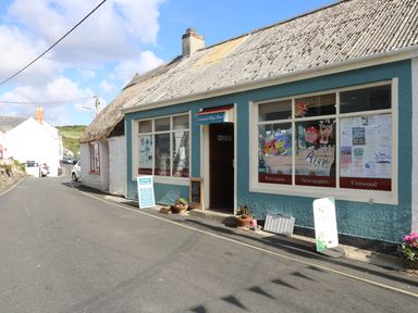 A street view featuring a small village store with a thatched roof and signs for provisions newspapers and firewood at Gannet Watch in Coverack
