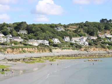 A beach with people walking near the water and houses on a hillside in the background at Gannet Watch in Coverack