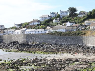 A rocky beach with a stone wall and white houses on a hillside at Gannet Watch in Coverack