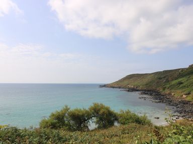 A coastal landscape with a grassy hillside and rocky shoreline overlooking the sea at Gannet Watch in Coverack