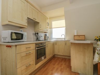 A kitchen with wooden cabinets a microwave oven a stove a kettle and a window with a blind at Gannet Watch in Coverack