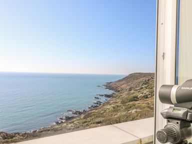 A coastal view of the sea and rocky cliffs with a telescope by a window at Gannet Watch in Coverack