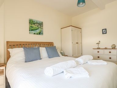 A bedroom with a wooden bed frame white bedding blue pillows white wardrobe and chest of drawers at Gannet Watch in Coverack