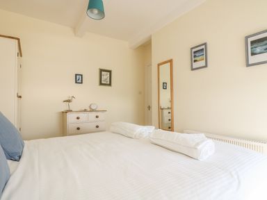 A bedroom with a bed with white linens and blue pillows a dresser a standing mirror and framed pictures on the walls at Gannet Watch in Coverack