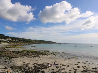 A beach with people sitting on towels and boats anchored in the water at Gannet Watch in Coverack