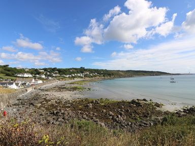A coastal village with houses along a rocky shoreline and boats in the water at Gannet Watch in Coverack