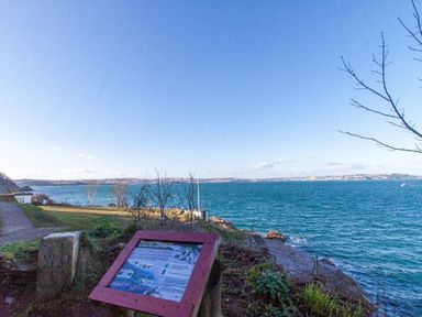A coastal view with a signboard near a walking path and blue sea at Bayview in Brixham