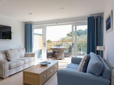 A living room with two sofas a wooden coffee table a wall-mounted TV and a balcony with outdoor furniture at Bayview in Brixham