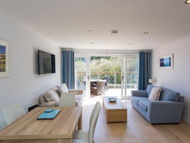 A living room with two sofas a wooden coffee table and dining table near glass doors at Bayview in Brixham