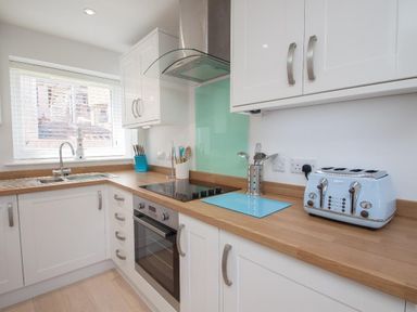 A kitchen with white cabinets wooden countertops a blue toaster and a window at Bayview in Brixham