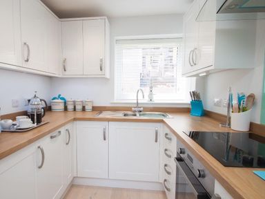 A kitchen with white cabinets wooden countertops a sink under a window and various kitchen utensils at Bayview in Brixham