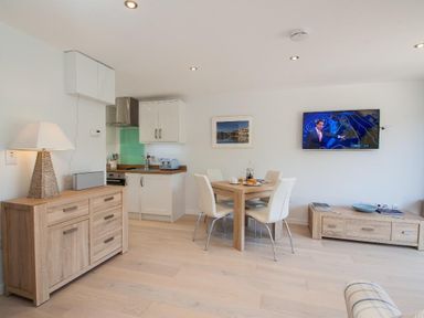 A dining area with a wooden table and white chairs next to a kitchen with white cabinets and wooden countertops at Bayview in Brixham