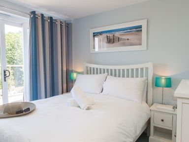 A bedroom with a white bed and pillows bedside tables with lamps and a framed beach picture above the bed at Bayview in Brixham