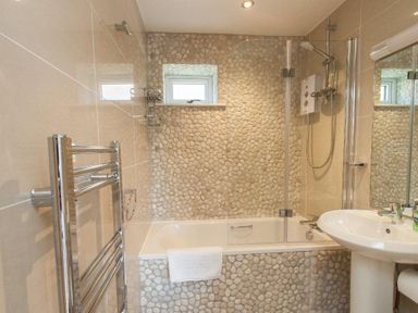 A bathroom with a bathtub shower and sink with pebble tiles at Bayview in Brixham