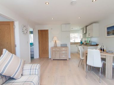 A living and dining area with a striped sofa wooden doors a wooden sideboard a dining table with white chairs and a kitchen with white cabinets at Bayview in Brixham