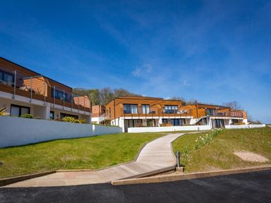 Modern apartment buildings with wooden balconies and glass railings on a grassy hill at Bayview in Brixham