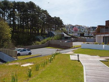 A parking area with cars next to a grassy lawn and wooden walkway with houses and trees in the background at Bayview in Brixham