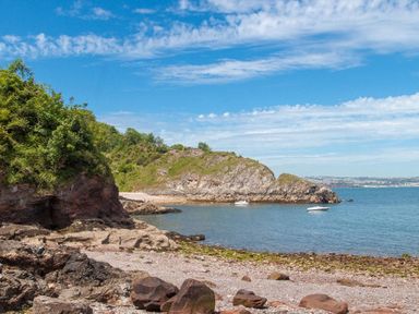 A rocky beach with green vegetation on cliffs and two boats on water at Bayview in Brixham