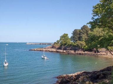 A coastal scene with two sailboats on the water and a rocky tree-lined shore at Bayview in Brixham