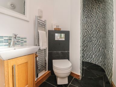 A bathroom with a toilet sink and a shower area with patterned tiles at Hay Loft Bolenowe Nr Portreath