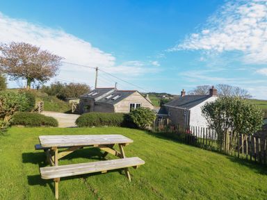 A wooden picnic table on grass with bushes and houses in the background at Hay Loft in Bolenowe Nr Portreath