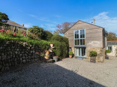 An exterior yard with a gravel surface a stone retaining wall with plants and flowers a wooden and stone two-story building at Hay Loft in Bolenowe Nr Portreath