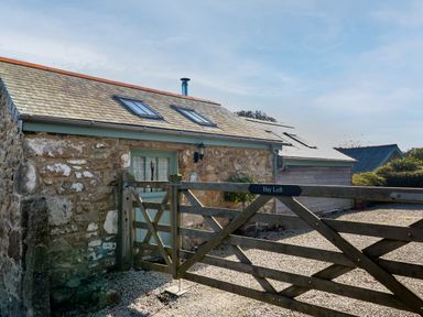 A stone building with skylights behind a wooden gate on a gravel driveway at Hay Loft Bolenowe Nr Portreath