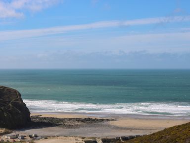 A beach with waves and rocky areas beside buildings near the shore at Hay Loft Bolenowe Nr Portreath