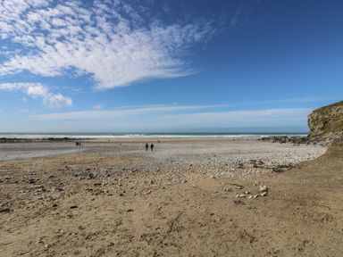 A sandy beach with scattered rocks people walking and a cliff on the right at Hay Loft Bolenowe Nr Portreath
