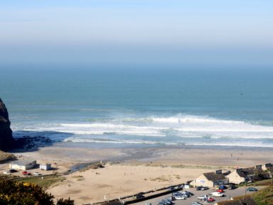 A sandy beach with waves hitting the shore a few buildings and parked cars near the beach at Hay Loft Bolenowe Nr Portreath
