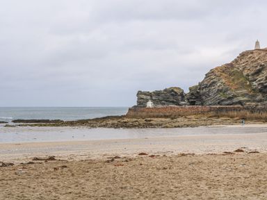 A sandy beach with rocky cliffs and a stone seawall at Hay Loft Bolenowe Nr Portreath