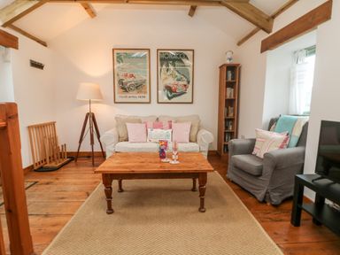 A living room with a beige sofa and gray armchair a wooden coffee table and framed posters on the wall at Hay Loft Bolenowe Nr Portreath